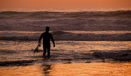 Rear view of man with surfboard at beach during sunset