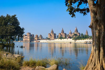 Buildings by lake against clear blue sky