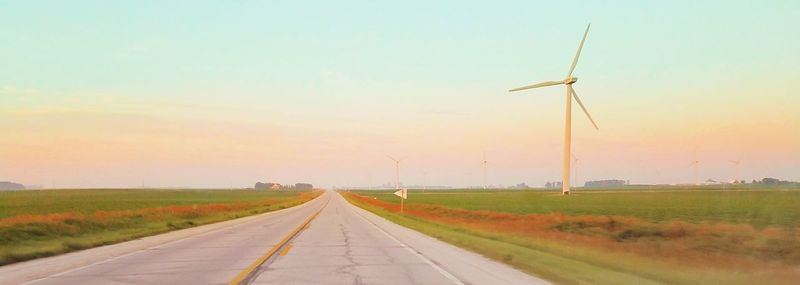 Wind turbines on field against sky during sunset