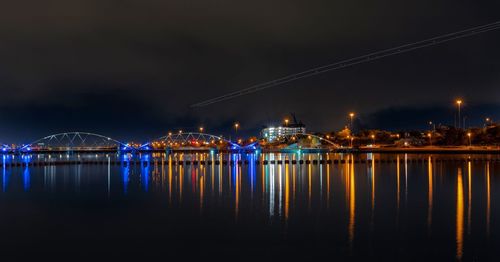 Illuminated bridge over river against sky at night