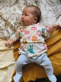 Portrait of a cute baby laying in the bed covered with ochre and beige covers and looking around 