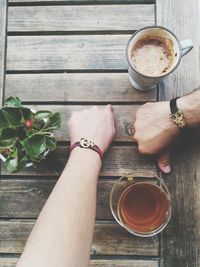 Close-up of people hands wearing bracelets by drinks on wooden table