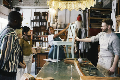 Male and female entrepreneurs showing upcycled wooden chair to customers at workshop