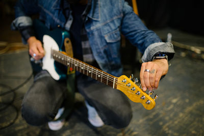 Young guitarist tuning his guitar closeup.