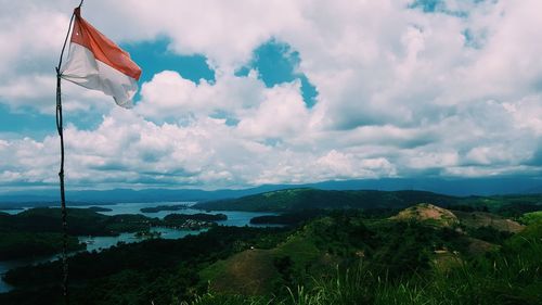 Indonesian flag on field by river against cloudy sky