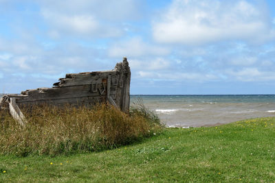 Wooden fence on grassy field by sea against sky