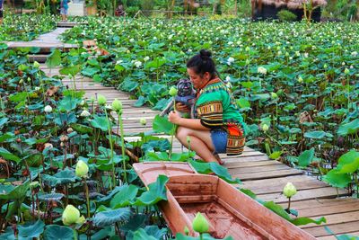 Full length of woman with dog crouching on pier over lake with flowering plants