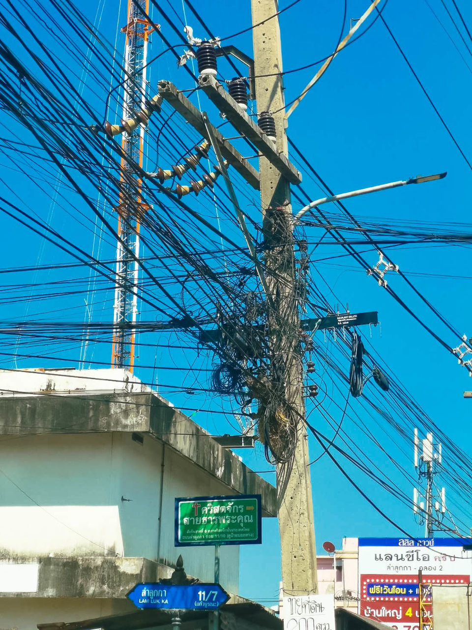 cable, electricity, architecture, power line, sky, transportation, vehicle, blue, built structure, day, nature, communication, mode of transportation, electricity pylon, sign, power supply, technology, no people, low angle view, city, building exterior, clear sky, power generation, outdoors, road, overhead power line, mast, street, text, urban area