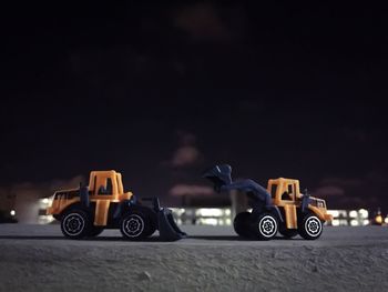 Close-up of toy earth movers on retaining wall against sky at night
