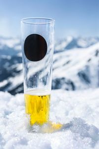 Close-up of  glass of beer cooling in the snow with a view of the mountain in the background.