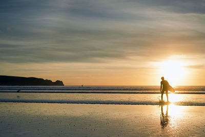 Silhouette surfer on beach against sky during sunset