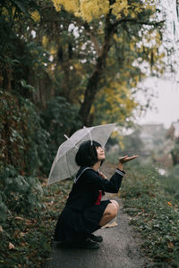 Side view of woman holding autumn leaf in forest