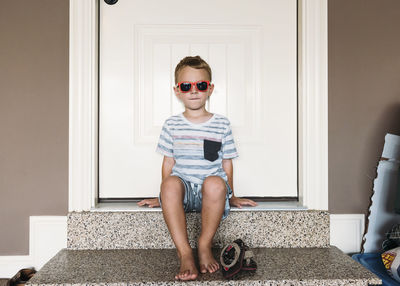 Full length of boy wearing sunglasses sitting on doorway