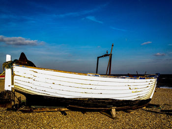 Abandoned boat moored on field against blue sky