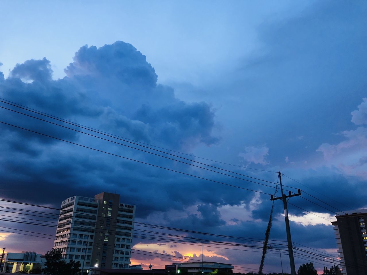 LOW ANGLE VIEW OF ELECTRICITY PYLON AMIDST BUILDINGS IN CITY