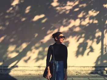 Smiling woman wearing sunglasses while standing against wall