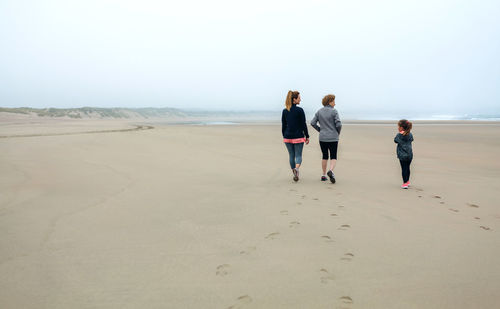 Rear view of women and girl walking on beach