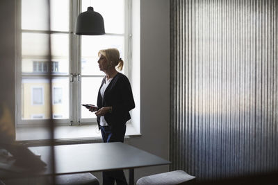 Senior businesswoman using mobile phone against window at creative office