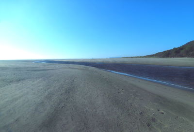 Scenic view of road by sea against clear blue sky