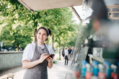 Happy young owner using smart phone while standing by food truck