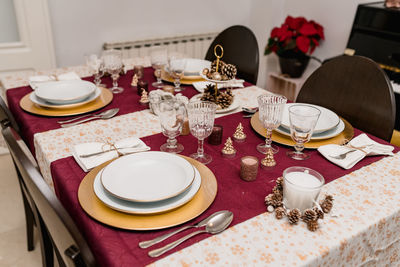 From above of table setting with glasses and cutlery near plates decorated with candles and cones for christmas celebration