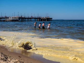 Rear view of people at beach against clear sky