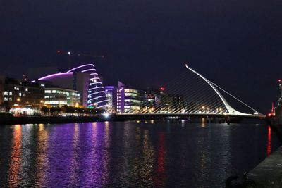 Illuminated city by river against sky at night