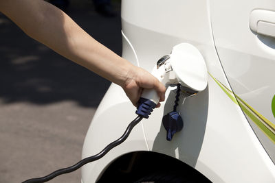 Cropped hand charging car at station