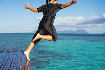 Full length of girl jumping in sea against sky