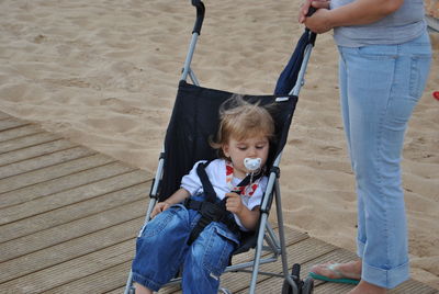 Low section of mother with son sitting on baby stroller at beach