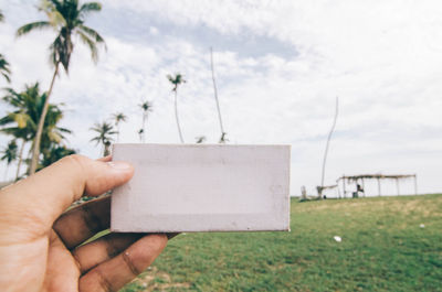 Cropped hand of man holding white box against cloudy sky