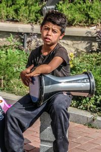 Portrait of boy playing drum on footpath during sunny day