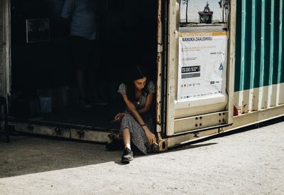 Full length of woman smoking cigarette while sitting in city