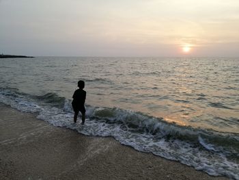 Rear view of man standing on beach during sunset