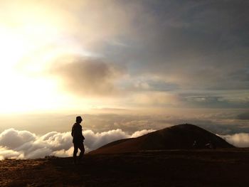 Silhouette man walking on landscape against sky during sunset