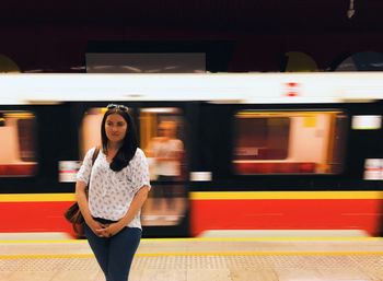 Young woman standing against blurred train at subway station