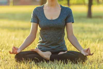 Low section of woman doing yoga on field