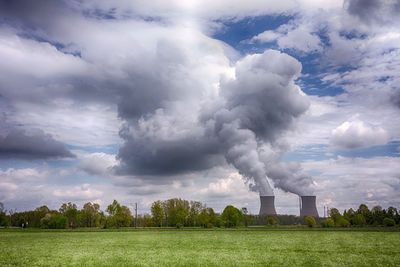 Smoke emitting from factory against cloudy sky