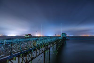 Pier over sea against cloudy sky at night