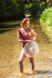 Full length of woman holding hat standing in water