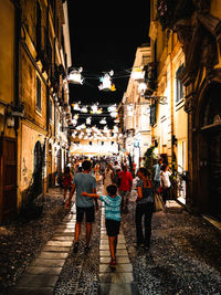 Rear view of people walking on street amidst buildings at night