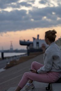 Friends sitting on retaining wall against sky during sunset
