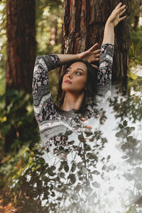 Woman standing by tree trunk in forest