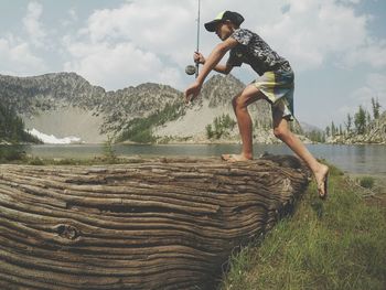 Full length of boy jumping on wood at lakeshore