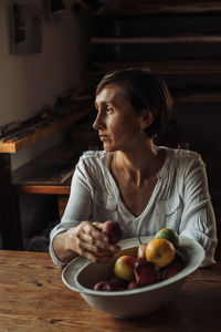 Middle aged woman sitting at table with bowl of fruits