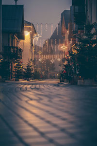 Illuminated street amidst buildings against sky at night