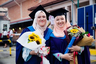 Portrait of smiling female friends standing in graduation gowns at university