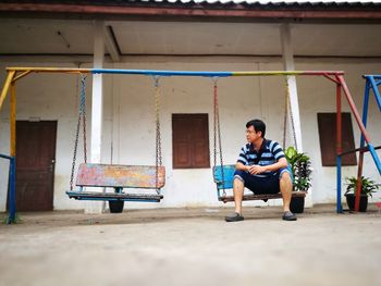Full length of man sitting on swing against building