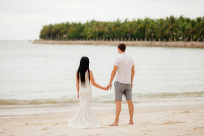 Rear view of couple holding hands while standing on beach