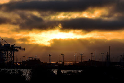 Silhouette cranes against orange sky during sunset